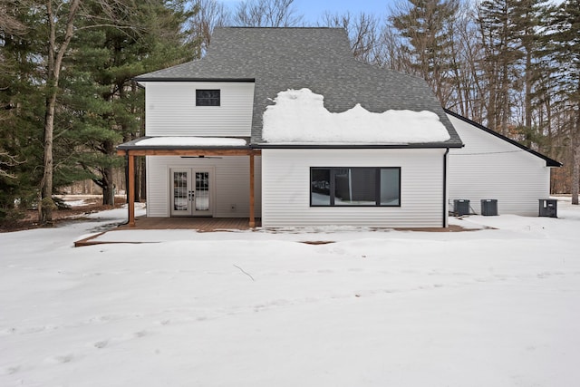 snow covered rear of property featuring french doors, roof with shingles, and central AC unit