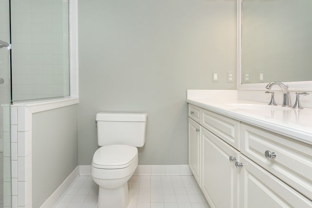 full bathroom with a tile shower, tile patterned flooring, toilet, vanity, and baseboards