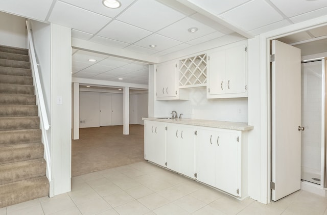 kitchen featuring a paneled ceiling, light colored carpet, light countertops, white cabinetry, and a sink