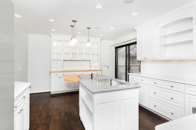 kitchen with dark wood finished floors, open shelves, backsplash, a sink, and a center island with sink