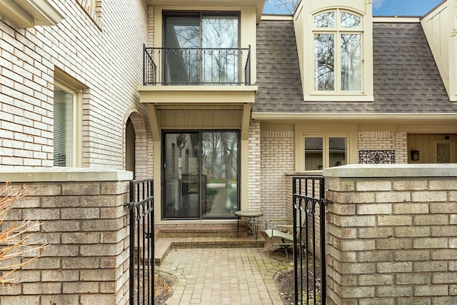 doorway to property with brick siding, a gate, roof with shingles, and mansard roof