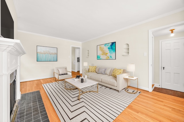 living room featuring light wood finished floors, a fireplace with flush hearth, baseboards, and crown molding