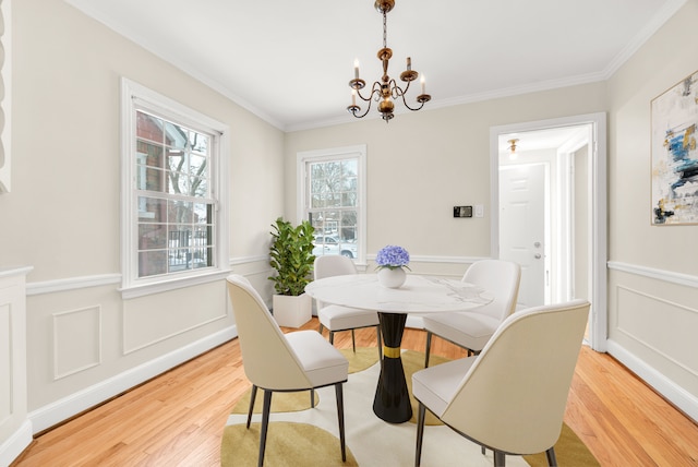 dining area with light wood-style floors, ornamental molding, a notable chandelier, and wainscoting