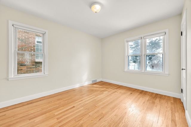 spare room featuring light wood-type flooring, visible vents, and baseboards