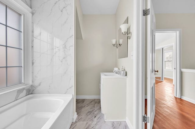 bathroom featuring marble finish floor, vanity, a bath, and baseboards