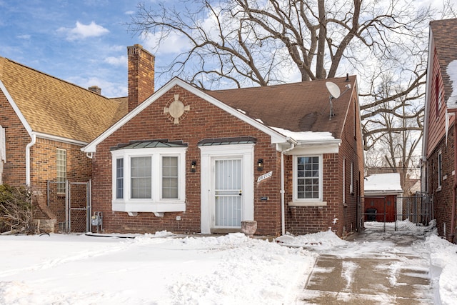 view of front facade featuring roof with shingles, a chimney, and brick siding