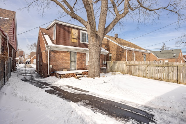 snow covered back of property featuring brick siding and fence private yard