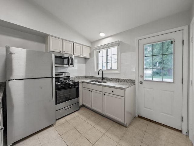 kitchen with stainless steel appliances, light countertops, light tile patterned flooring, vaulted ceiling, and a sink