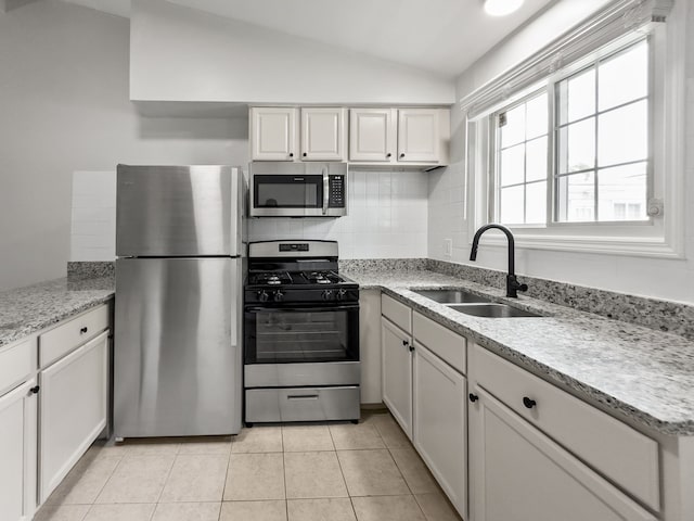 kitchen featuring lofted ceiling, light tile patterned floors, stainless steel appliances, a sink, and white cabinetry