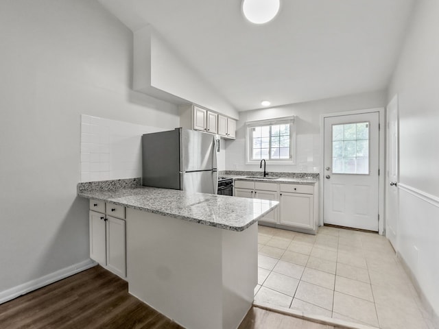 kitchen featuring light stone counters, a peninsula, a sink, white cabinets, and freestanding refrigerator