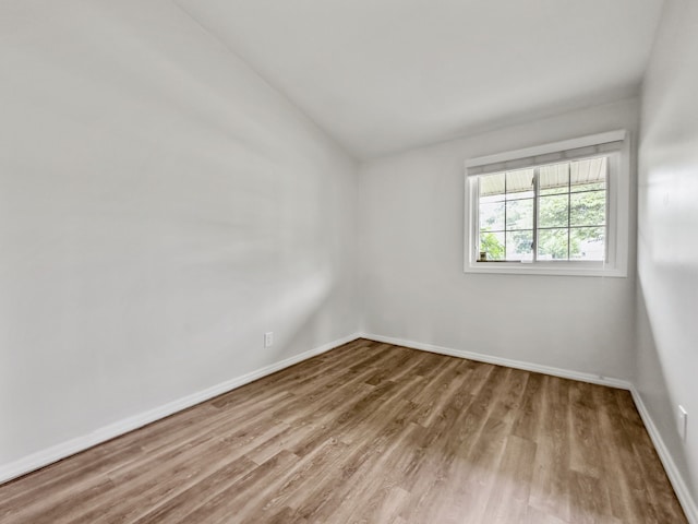 spare room with vaulted ceiling, light wood finished floors, and baseboards