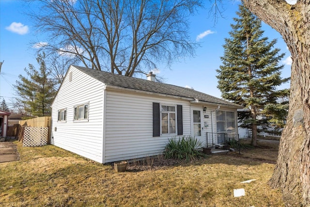 view of front facade with a shingled roof, a front yard, fence, and a chimney