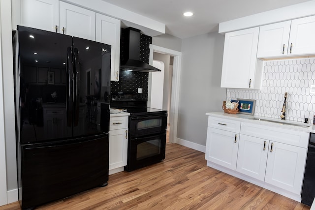 kitchen featuring wall chimney range hood, light countertops, black appliances, white cabinetry, and a sink