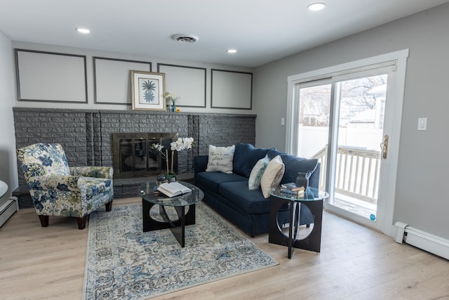 living area with recessed lighting, visible vents, light wood-style flooring, a baseboard heating unit, and a brick fireplace