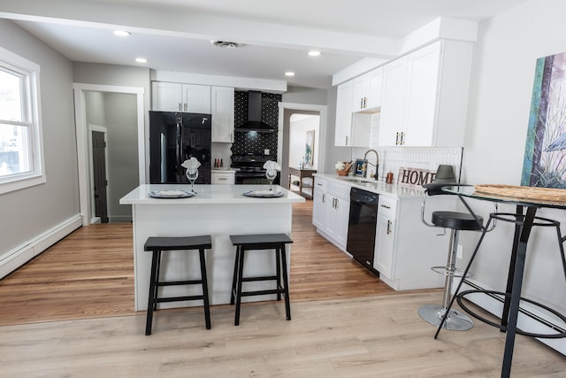 kitchen with a center island, white cabinets, a sink, black appliances, and wall chimney exhaust hood