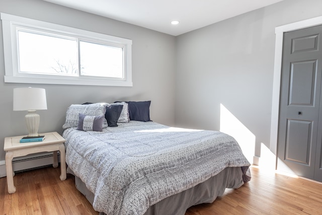 bedroom with light wood finished floors, a baseboard radiator, and recessed lighting