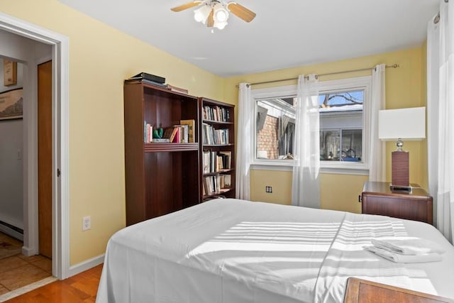 bedroom with baseboards, baseboard heating, a ceiling fan, and light wood-style floors