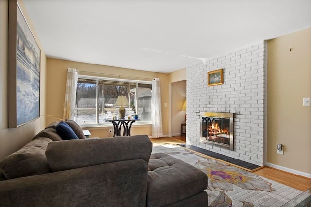 living room with a brick fireplace, baseboards, and light wood-style floors