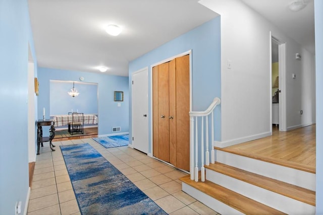 corridor featuring visible vents, stairway, light tile patterned flooring, a chandelier, and baseboards