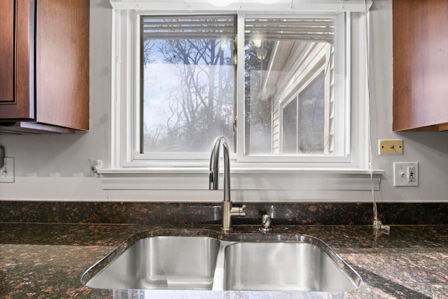 kitchen with dark stone countertops, brown cabinetry, and a sink