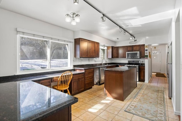 kitchen with light tile patterned floors, dark stone counters, a kitchen island, stainless steel appliances, and a sink