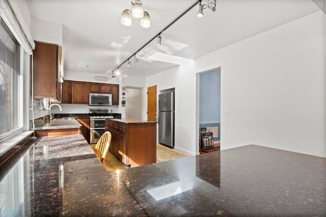 kitchen featuring a center island, brown cabinets, stainless steel appliances, a sink, and track lighting