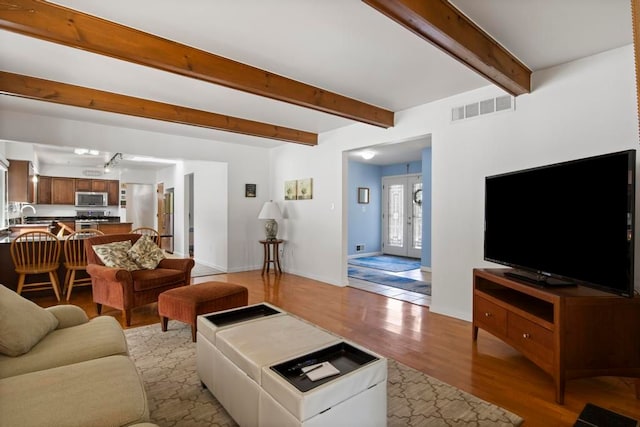 living room featuring baseboards, visible vents, light wood-style flooring, french doors, and beam ceiling