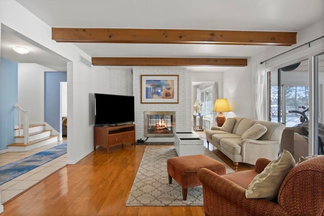 living room with a fireplace, visible vents, light wood-style floors, stairway, and beam ceiling