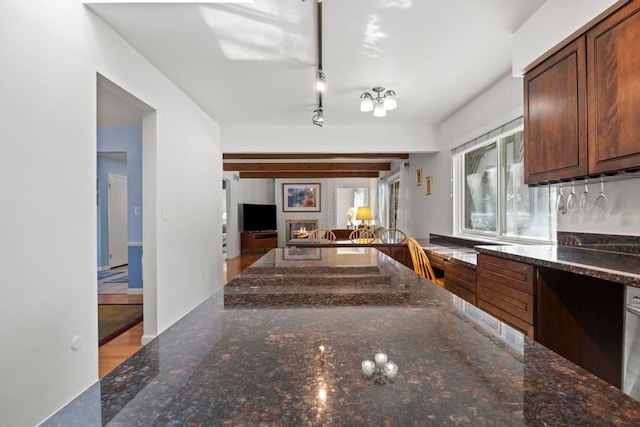 kitchen with open floor plan, dark stone counters, a brick fireplace, and track lighting