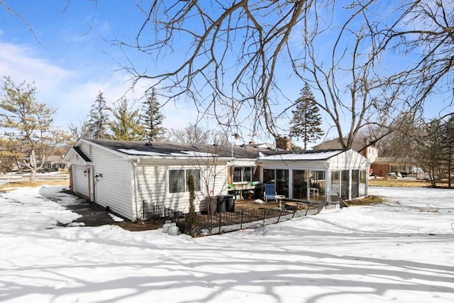 snow covered rear of property with a sunroom