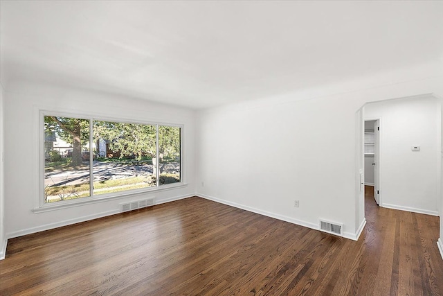 unfurnished room with visible vents, dark wood finished floors, and baseboards