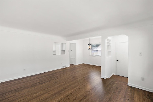 unfurnished room with dark wood-style floors, arched walkways, visible vents, and baseboards