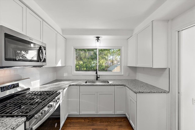 kitchen featuring appliances with stainless steel finishes, white cabinets, a sink, and light stone countertops