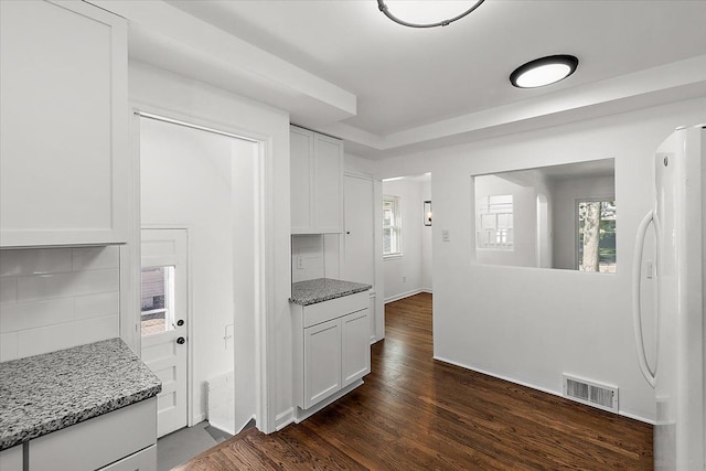 kitchen with light stone counters, visible vents, white cabinetry, freestanding refrigerator, and dark wood finished floors