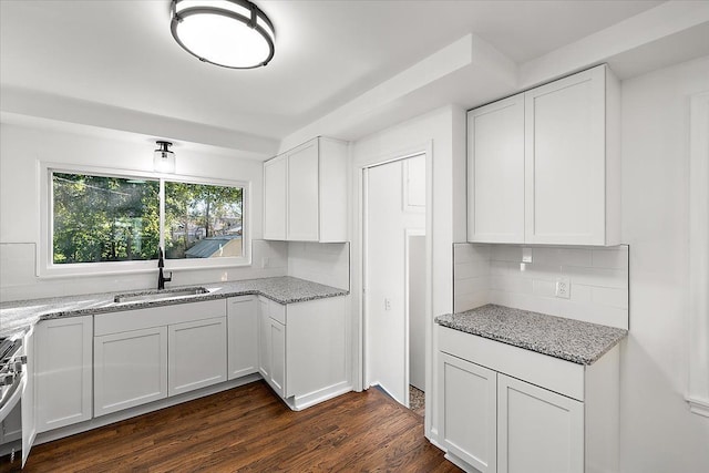 kitchen featuring dark wood-style floors, stove, light stone countertops, white cabinetry, and a sink