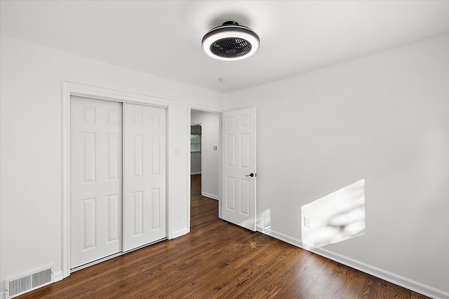 unfurnished bedroom featuring dark wood-type flooring, a closet, visible vents, and baseboards