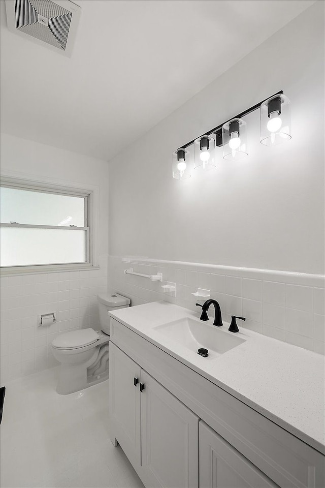 half bath with visible vents, toilet, a wainscoted wall, vanity, and tile walls