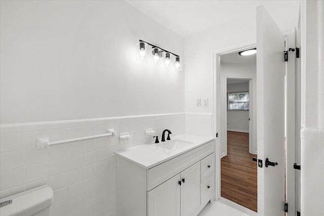 half bathroom with toilet, a wainscoted wall, wood finished floors, vanity, and tile walls