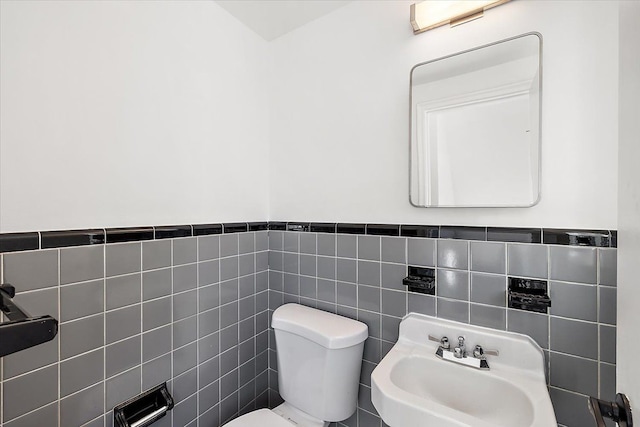 half bathroom with toilet, a wainscoted wall, tile walls, and a sink