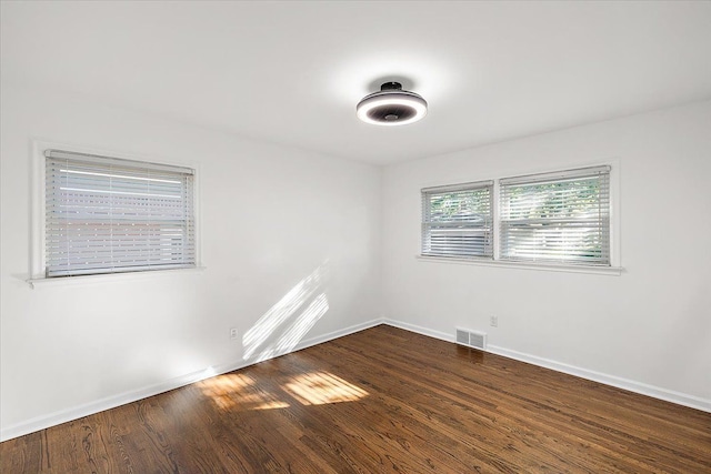 unfurnished room featuring dark wood-style flooring, visible vents, and baseboards