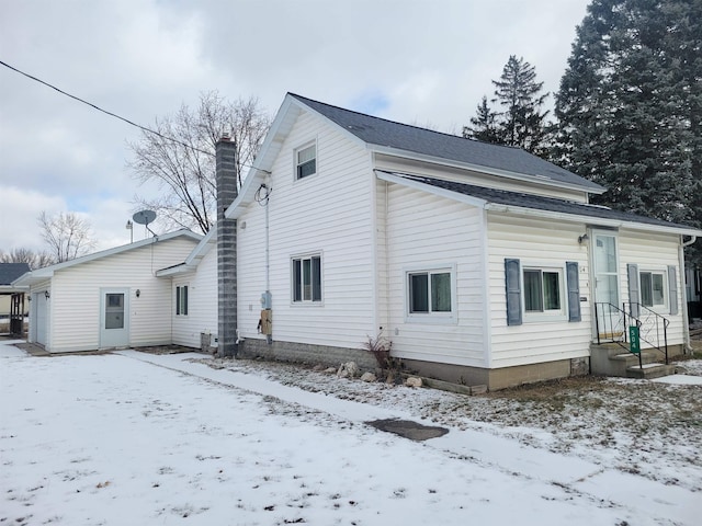 snow covered rear of property featuring a chimney