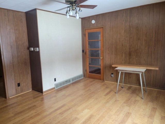 spare room with ceiling fan, wood walls, light wood-type flooring, and visible vents