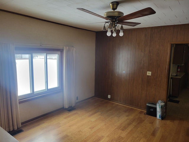 spare room with baseboards, visible vents, a ceiling fan, crown molding, and light wood-style floors