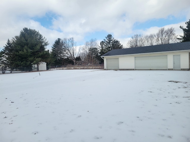 yard covered in snow featuring an outbuilding, a detached garage, a storage shed, and fence