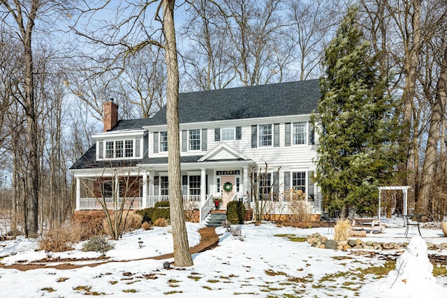 view of front facade featuring covered porch, a shingled roof, and a chimney