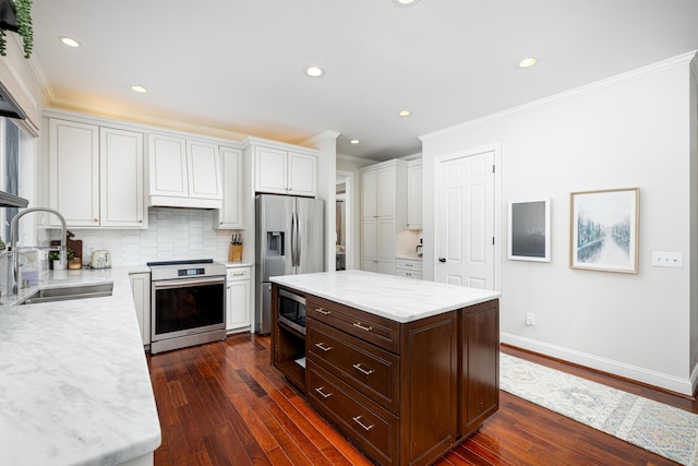 kitchen with crown molding, stainless steel appliances, white cabinets, a sink, and a kitchen island