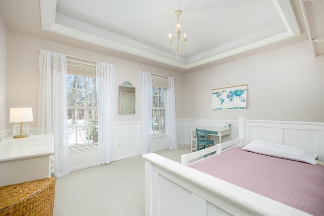 bedroom featuring a raised ceiling, light colored carpet, a notable chandelier, and a wainscoted wall