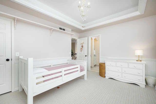 bedroom with a tray ceiling, a wainscoted wall, light colored carpet, visible vents, and an inviting chandelier