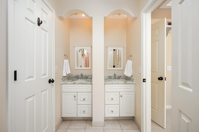 bathroom featuring tile patterned flooring, two vanities, a sink, and baseboards