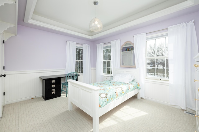 bedroom featuring a raised ceiling, multiple windows, light carpet, and wainscoting